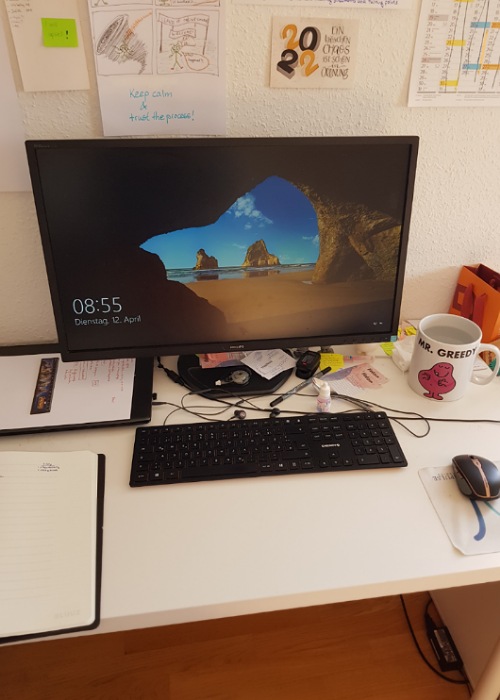 Ein Blick auf meinen Schreibtisch: Der Bildschirm ist schon eingeschaltet und zeigt einen ganz klassischen Bildschirmschoner mit Strand-Bild.
